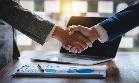 two professionals shaking hands over documents and a laptop